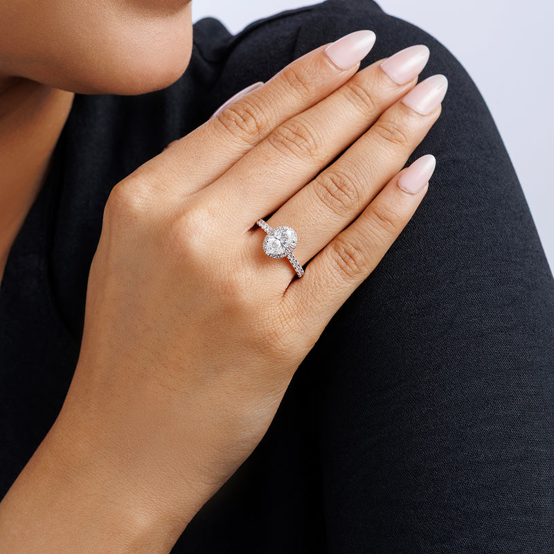 A woman's hand with light pink nails showcases the Keemti Jewels CLASSIC Oval Mount Solitaire Ring against her black sleeve.