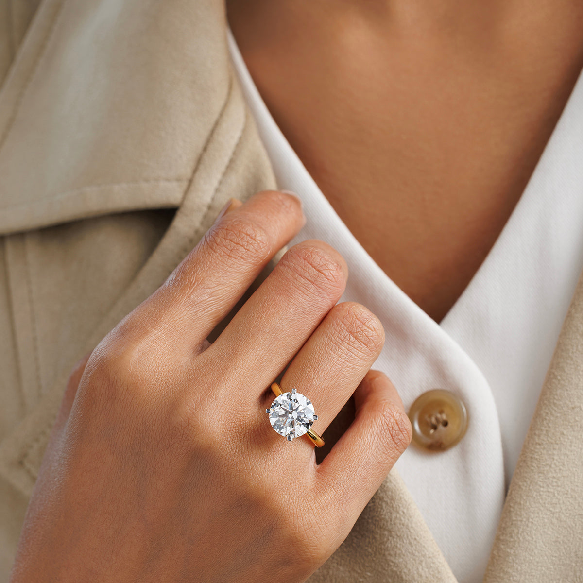 A hand wears the Keemti Jewels ELEGANT Round Solitaire RING on a gold band, over a beige coat and white top.