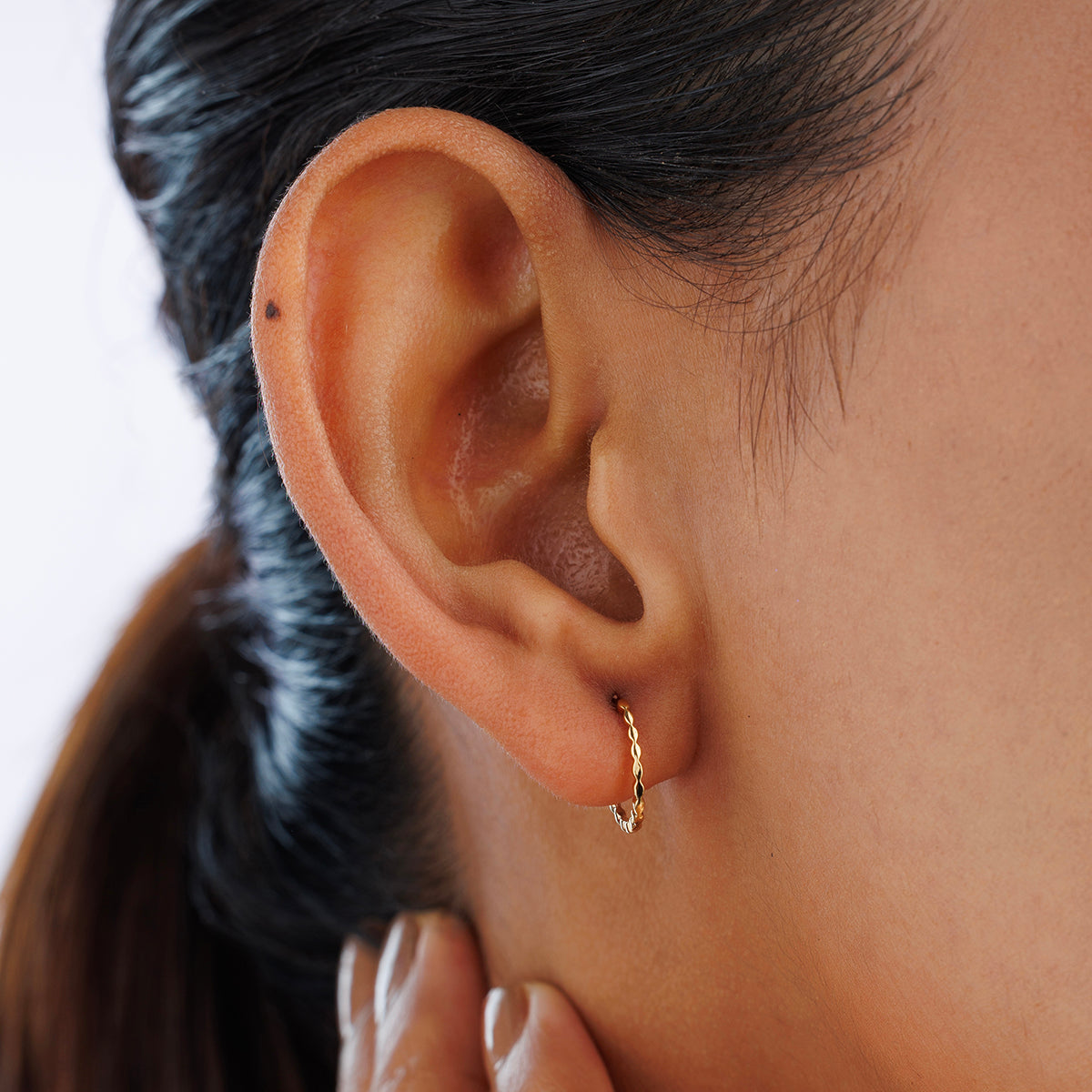 Gold-tone textured hoop earrings worn on ear, twisted detail visible