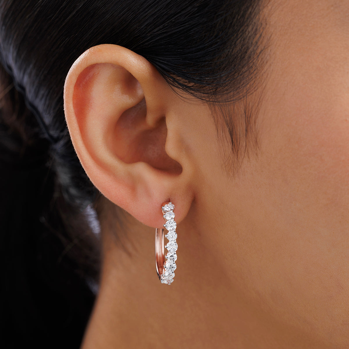 Close-up of a woman's ear wearing Keemti Jewels LINEAR Weave Huggie Earrings in elegant rose gold with white gemstones.