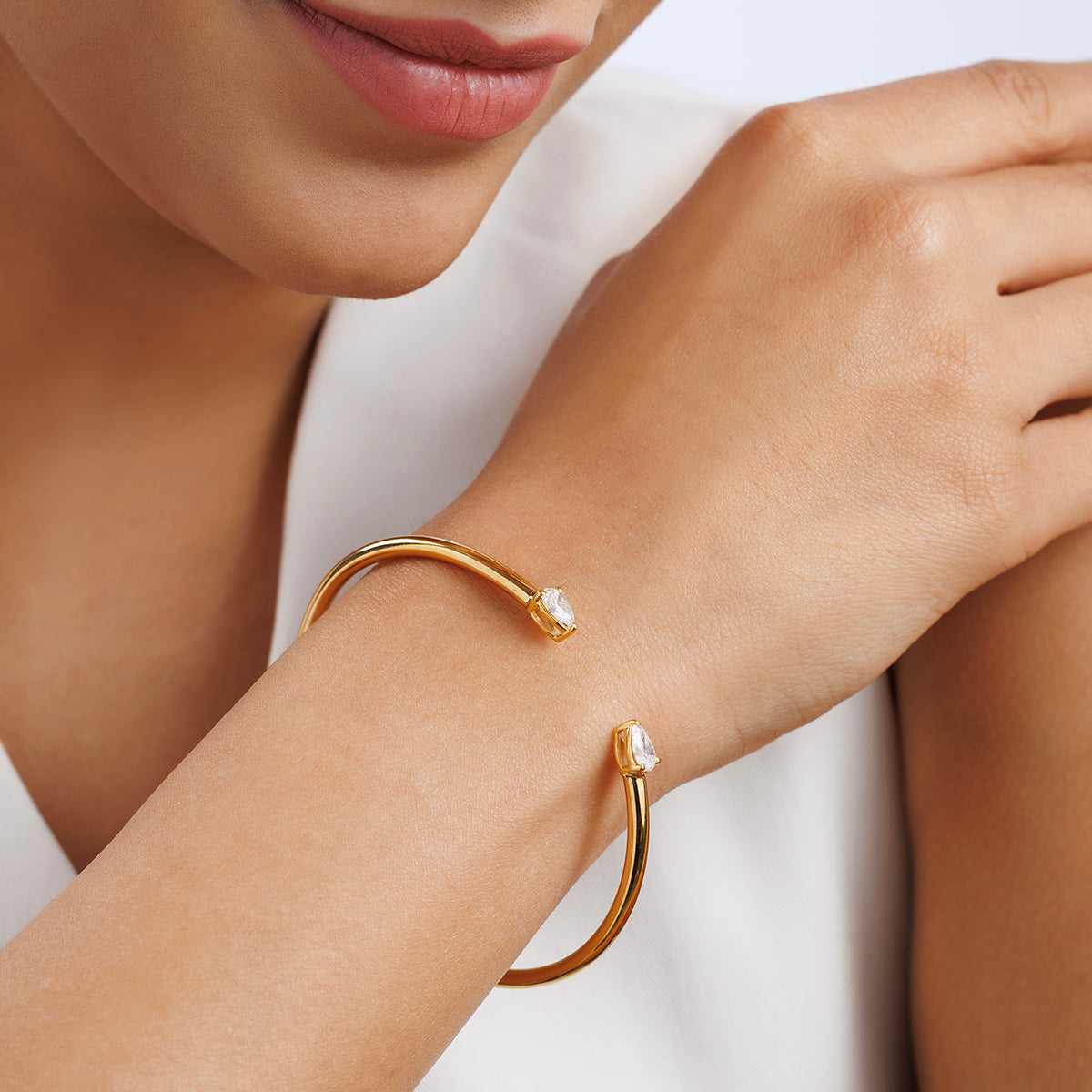 A woman pairs a white top with the Keemti Jewels PEAR Luxe BRACELET, featuring gold curves and clear gemstones.