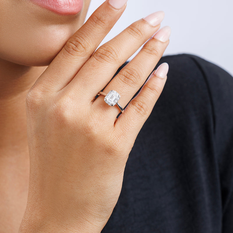 A woman's hand with Keemti Jewels' EMERA Halo Solitaire ring, pavé-set diamonds, near her lips.