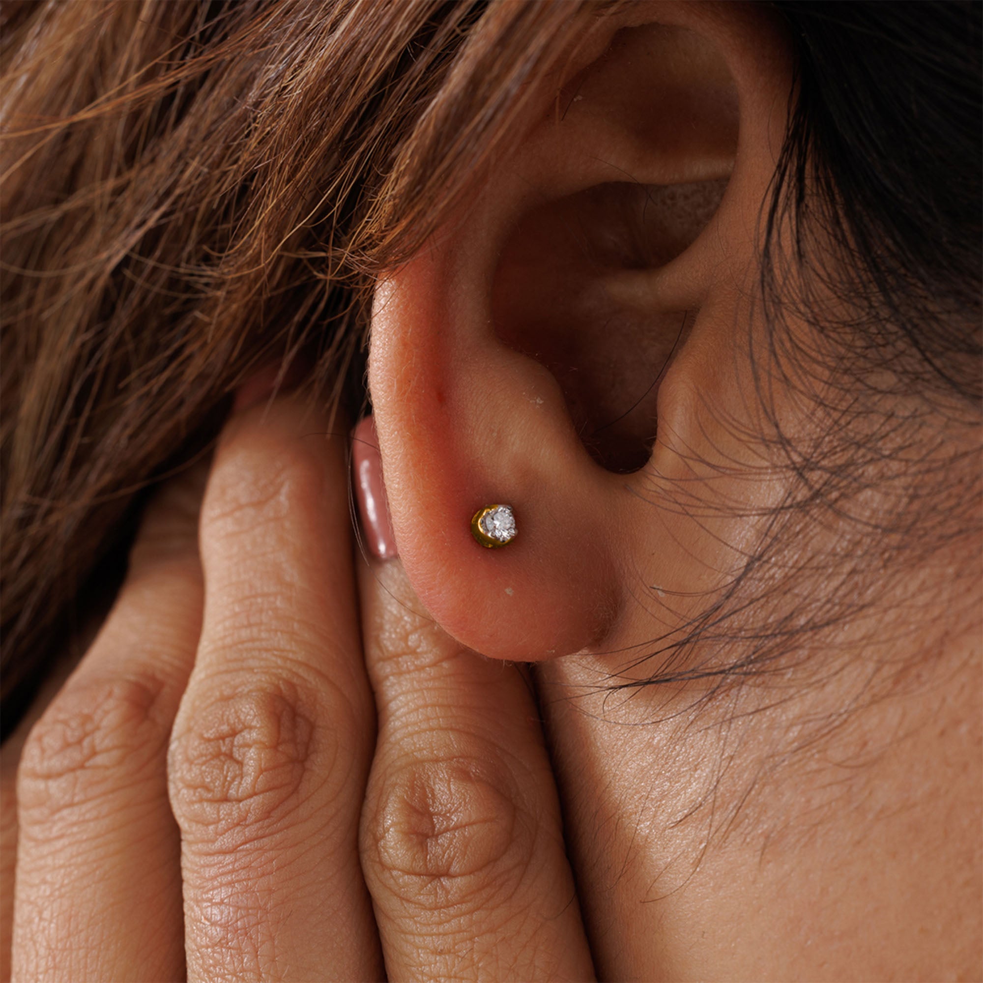 Close-up of ear with Keemti Jewels' Everyday Glow Solitaire Stud Earring; hand tucks hair by the minimal piece.