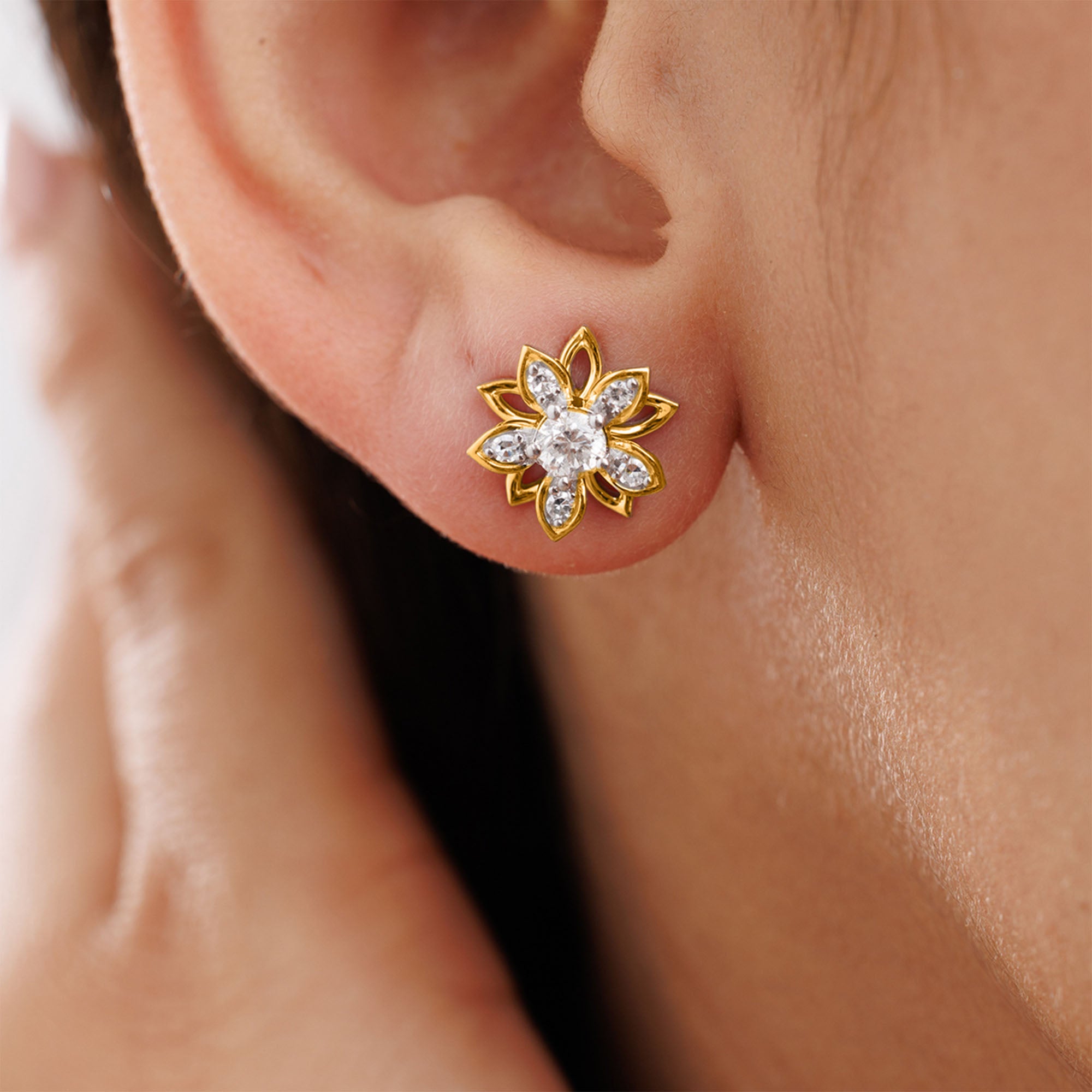 A close-up of an ear wearing Keemti Jewels’ Golden Mirage Bloom Stud Earrings with clear gemstone and petal accents.