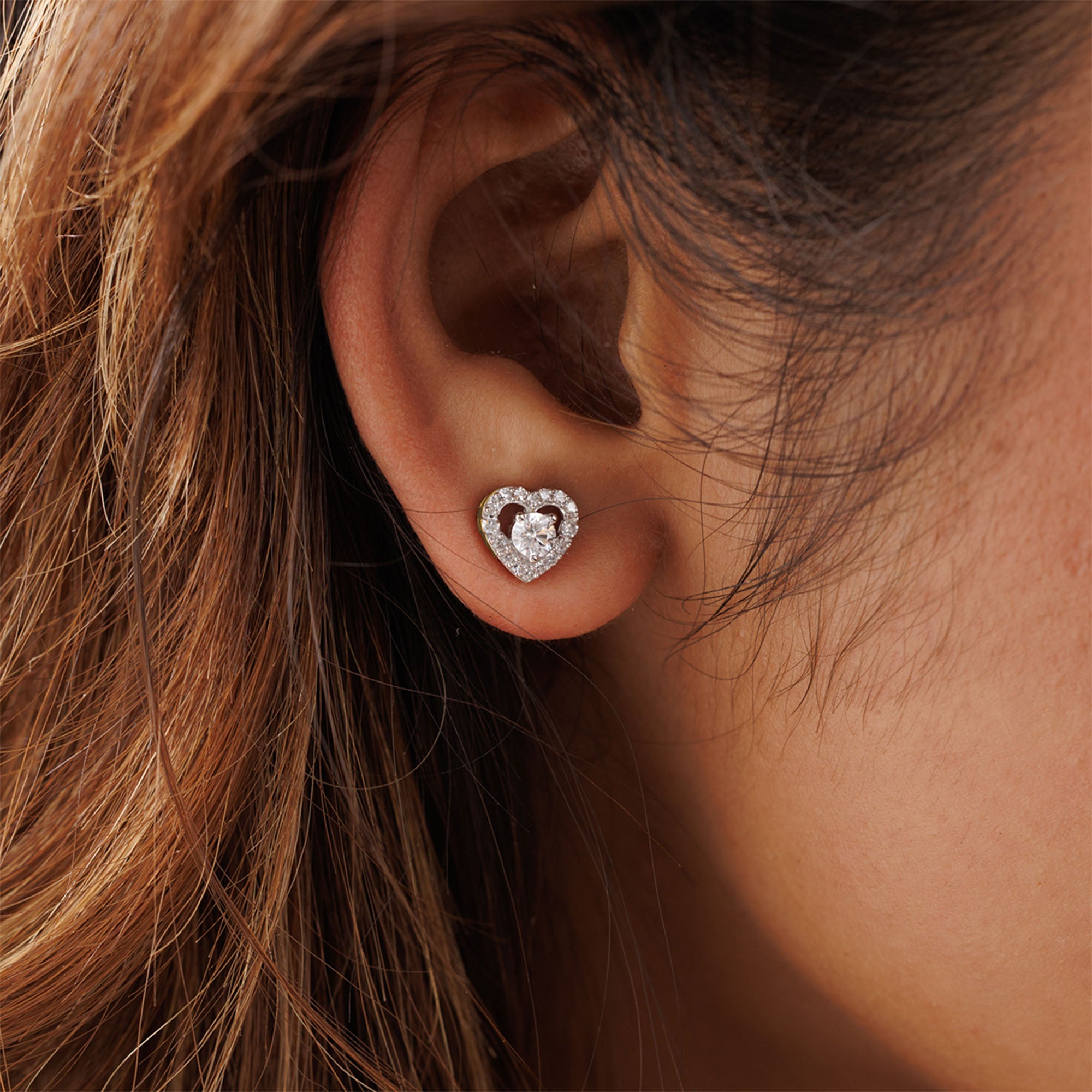 A close-up of an ear with brown hair wearing Keemti Jewels' Solitaire Center Stone Heart Stud Earrings.