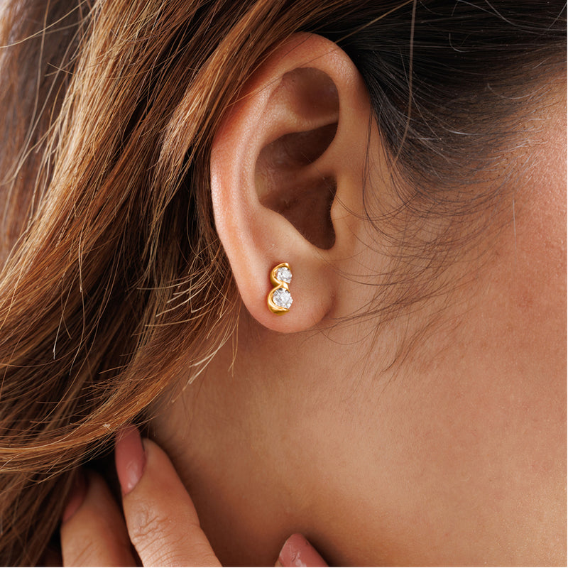 A hand brushes hair near an ear adorned with Keemti Jewels' Twin Spark Stud Earrings, shining with harmonious sparkle.