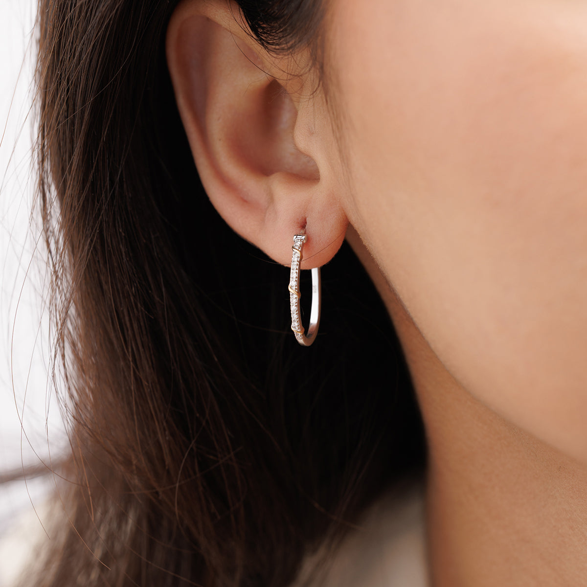 Close-up of a woman's ear with Keemti Jewels' Eternal Entwine Hoop Earrings, featuring dual-tone and gemstone accents.