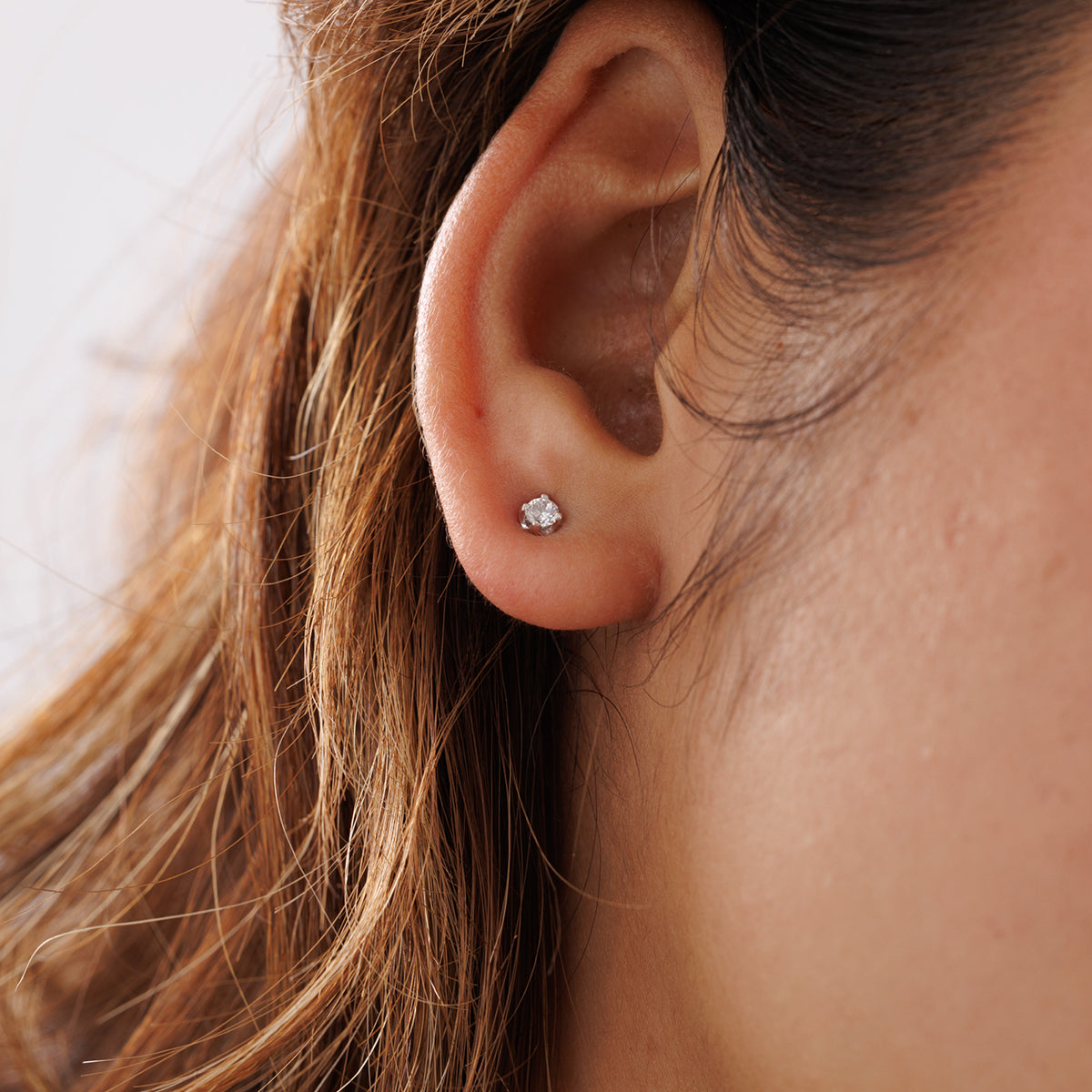 A close-up of a person’s ear wearing Keemti Jewels’ Morning Dew Diamond Stud Earrings in elegant white metal.