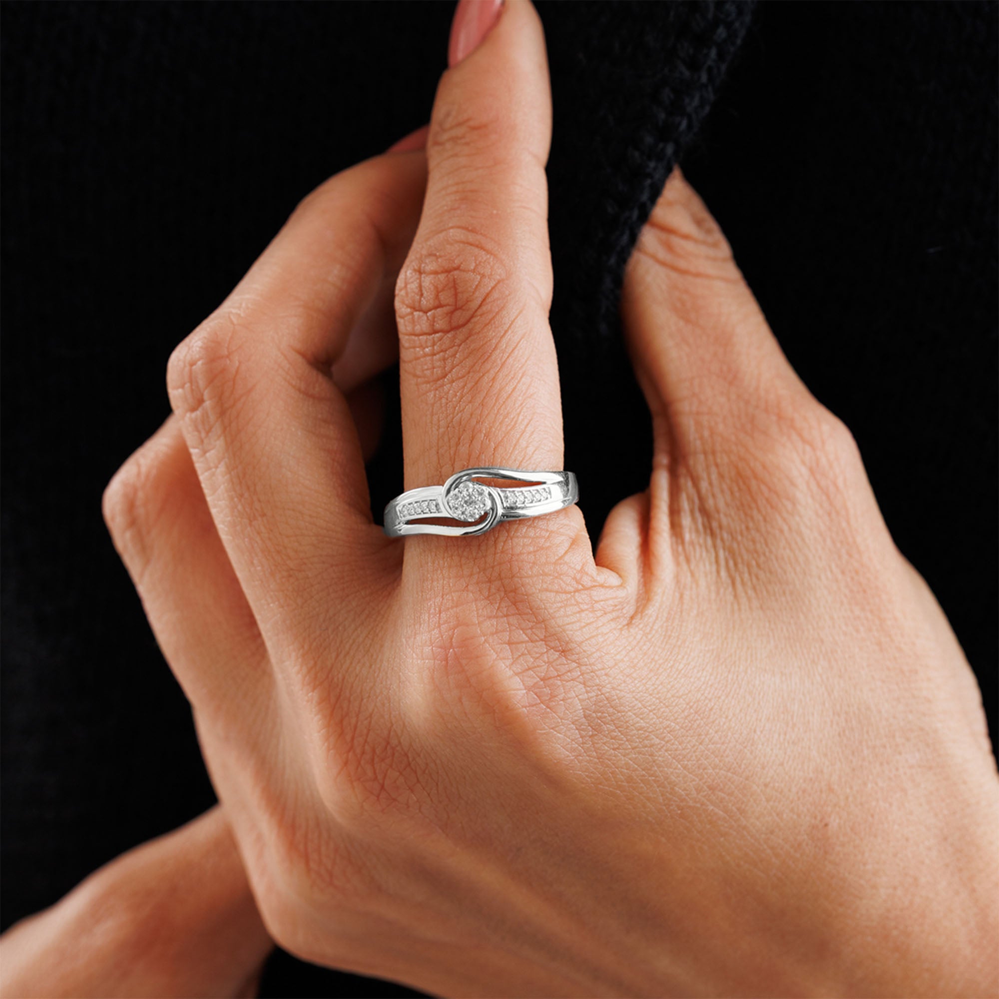 A hand with Keemti Jewels' Loop Of Light Diamond Ring, unity style, set with diamonds, holds dark fabric.