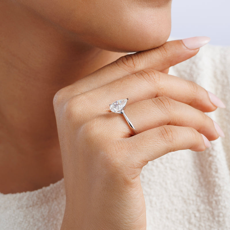 A hand with neatly manicured nails wears the Keemti Jewels EVERDEW Pear Solitaire RING, resting on a woman’s chin.