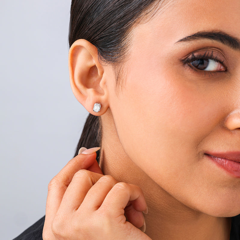 A woman wearing Keemti Jewels’ Modern Emerald-Cut Halo Diamond Stud Earrings smiles and gently touches her ear.