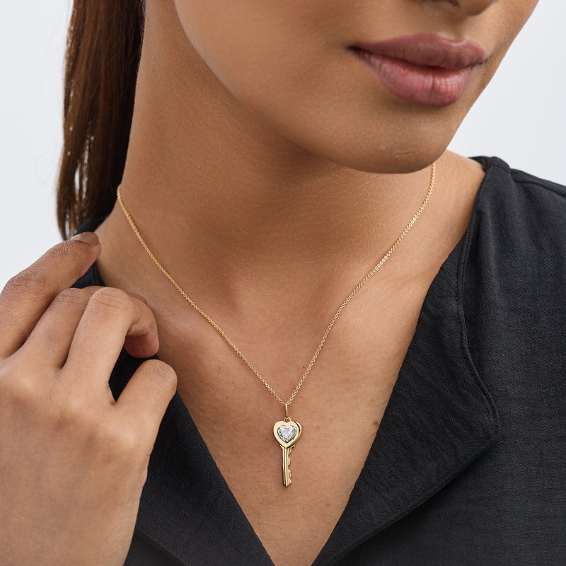 Woman in a black top wears Keemti Jewels' Key To My Heart Diamond Necklet, a gold heart-key with a clear stone.