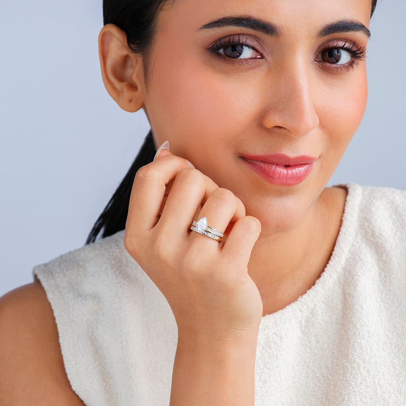 A woman models Keemti Jewels' Soft Glow Pear Diamond Solitaire Ring on a gold band, smiling gently at the camera.