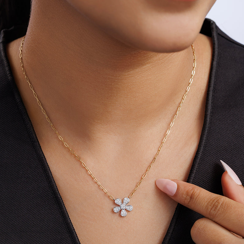 A woman points to the DAISY Sparkle NECKLET by Keemti Jewels, featuring a diamond flower pendant.