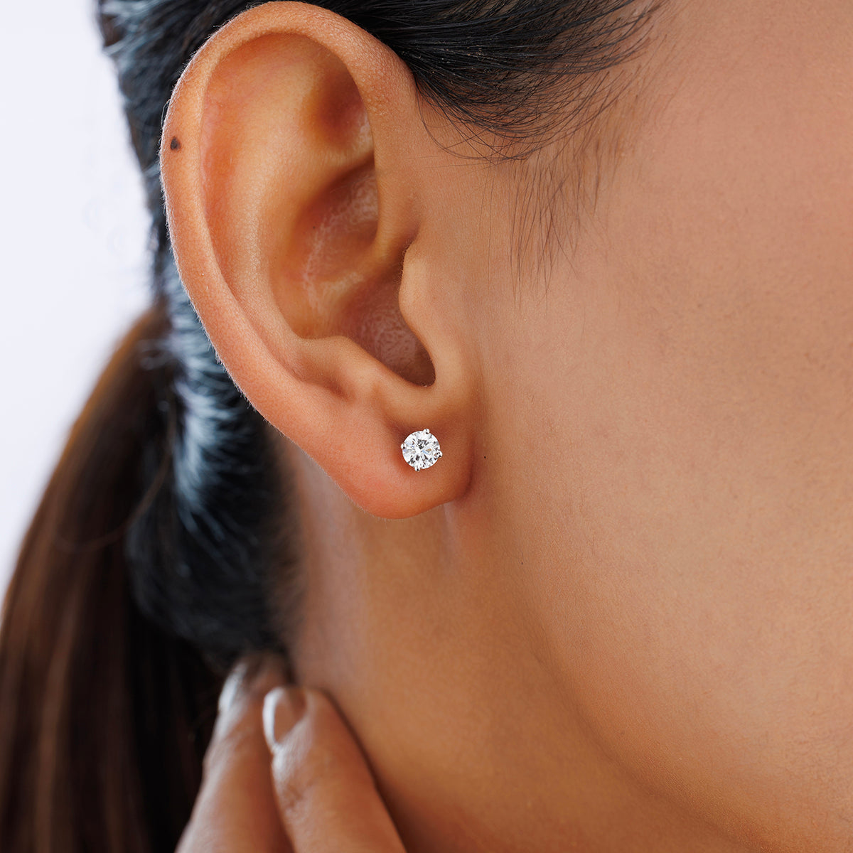 A woman wears Keemti Jewels TIMELESS Solitaire Stud Earrings, sparkling in a classic four-prong setting.