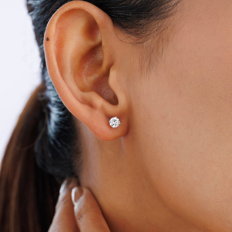 A woman wears Keemti Jewels TIMELESS Solitaire Stud Earrings, sparkling in a classic four-prong setting.