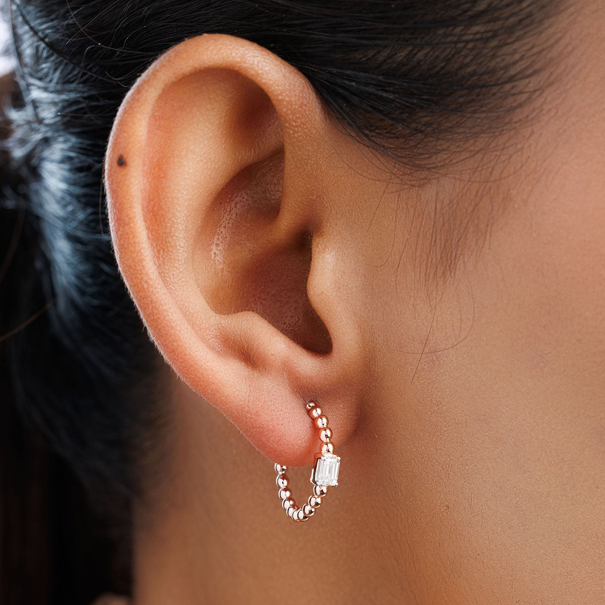 Hoop earrings on ear: rose-gold beaded ring with rectangular clear centerpiece stone