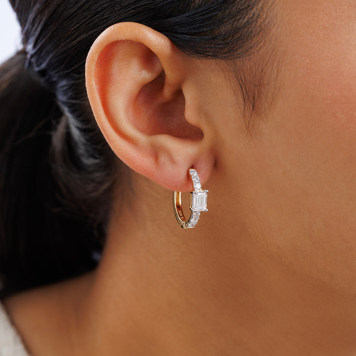 Close-up of a woman's ear wearing Keemti Jewels AERIS Emerald Huggie Earrings with small diamonds.