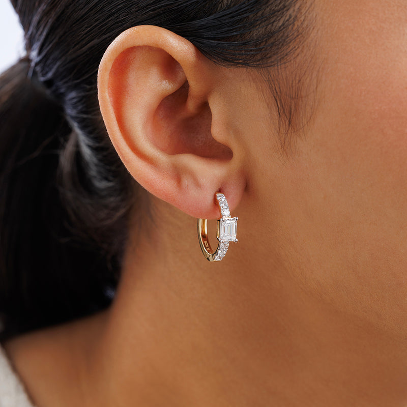 Close-up of a woman's ear wearing Keemti Jewels AERIS Emerald Huggie Earrings with small diamonds.