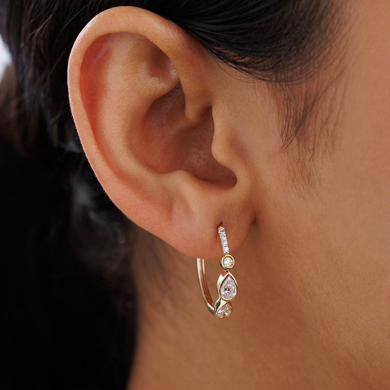 Diamond hoop earrings worn on ear, yellow gold with pear-shaped drops