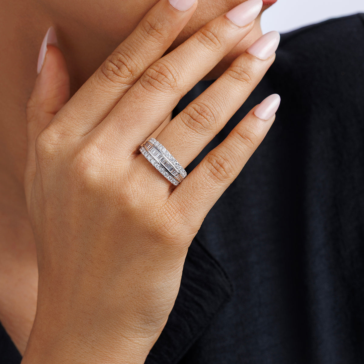A hand with light pink nails wears the Keemti Jewels LAYERED Spark Diamond BAND, stacked near the face on dark fabric.