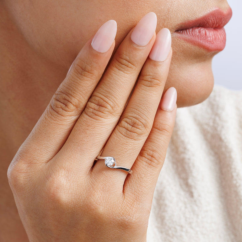 A woman with manicured nails wears the Keemti Jewels RADIANT Swirl RING, its diamond gleaming on her finger.