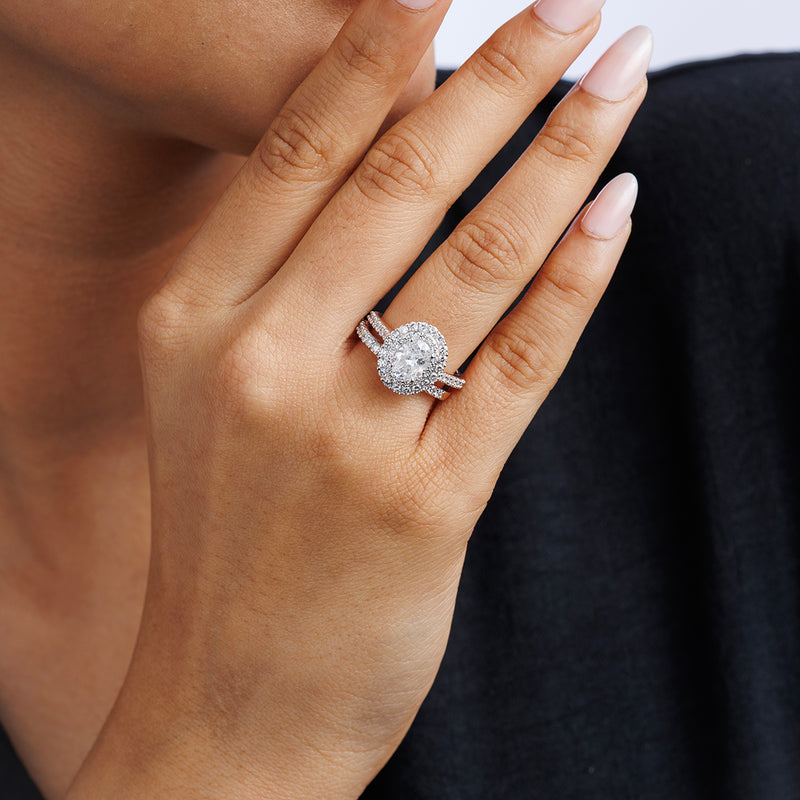 A hand with nude nails wears the Keemti Jewels ETERNAL Glow Oval Halo Ring, set against a dark background.