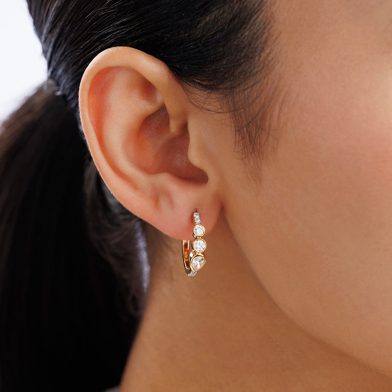 Close-up of a woman's ear wearing Keemti Jewels AERIS Marquise Huggie Earrings—gold hoops with clear gemstones.