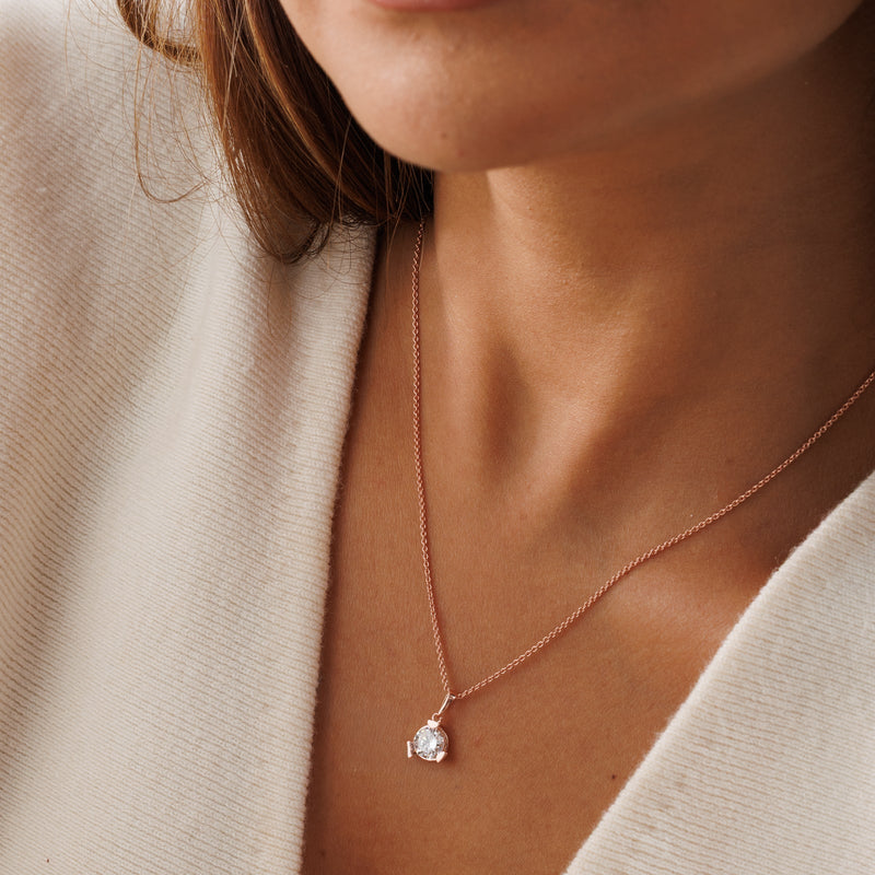 Rose-gold diamond necklet worn close-up; round pendant on fine chain