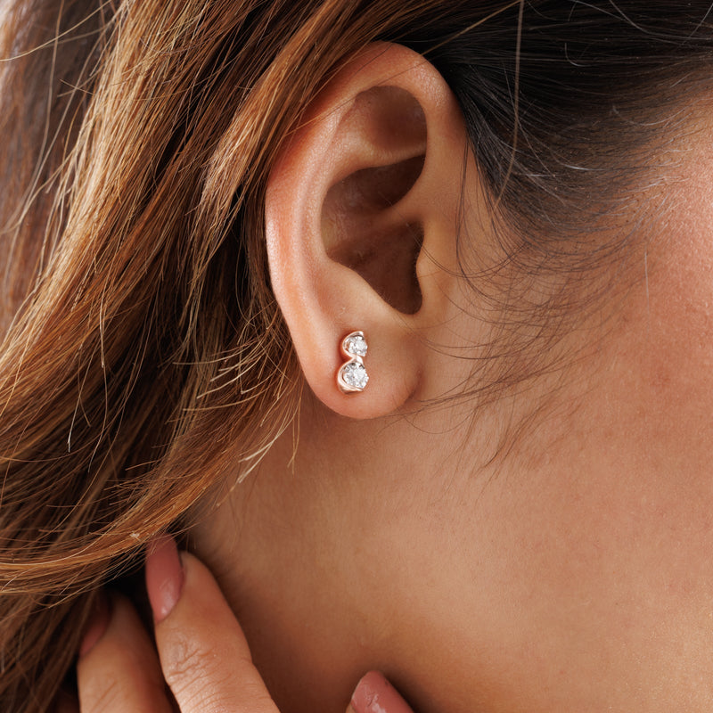 Twin spark stud earrings on ear: two small round clear stones in rose-gold settings