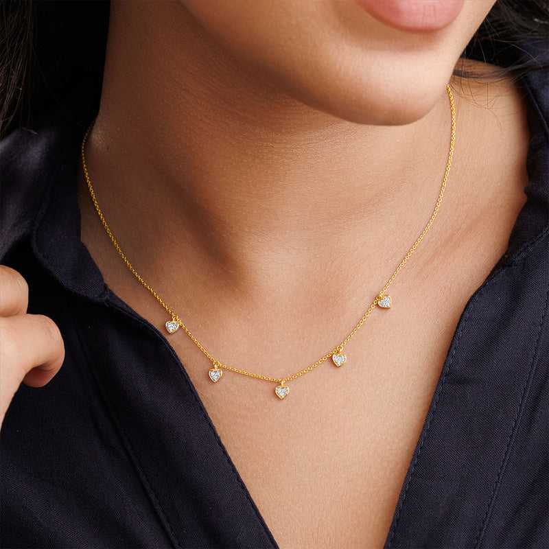 A woman wears a Keemti Jewels Linked By Love Charm Necklet with five hearts over a dark blue collared shirt.