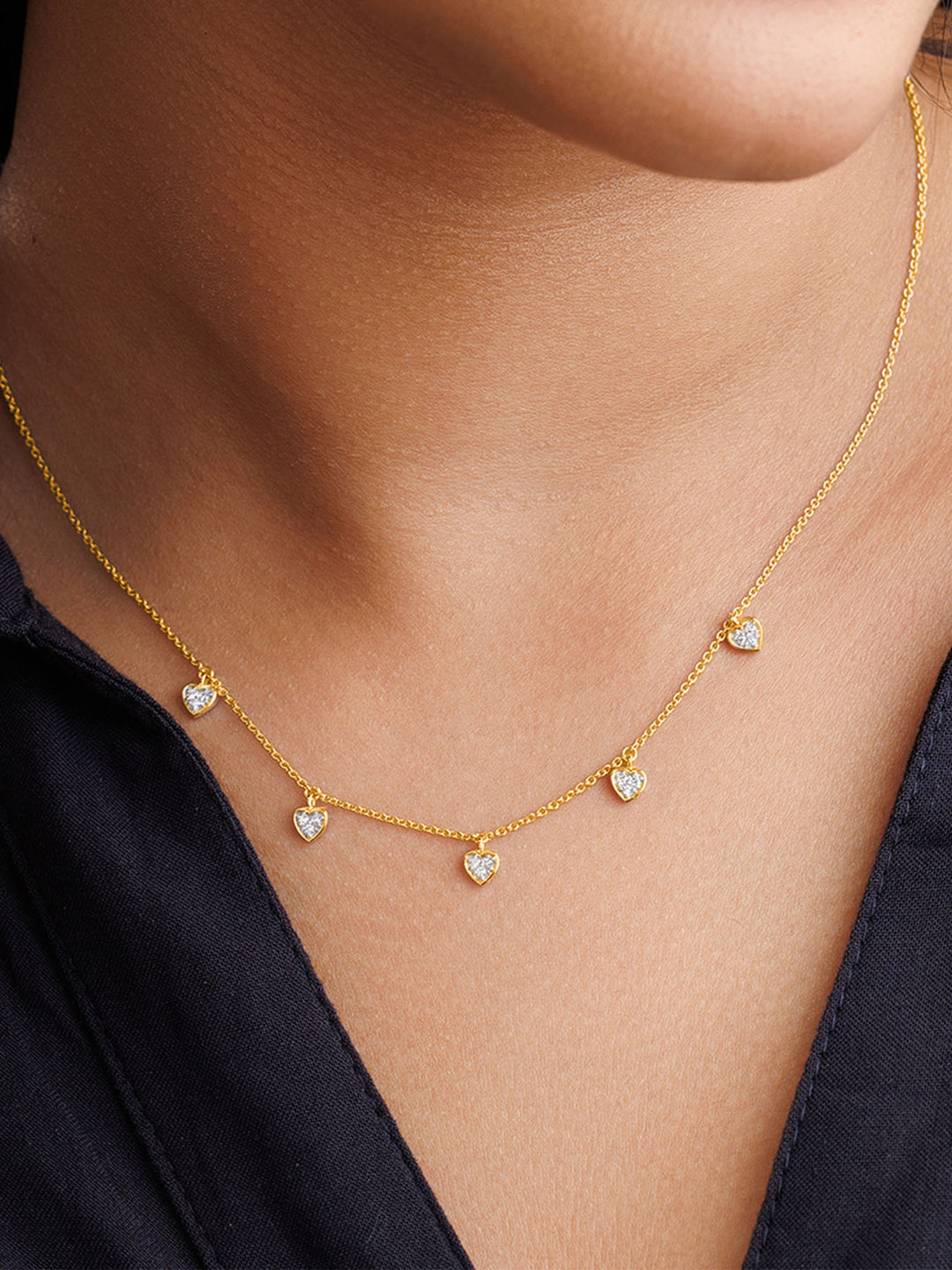 A woman wears a Keemti Jewels Linked By Love Charm Necklet with five hearts over a dark blue collared shirt.