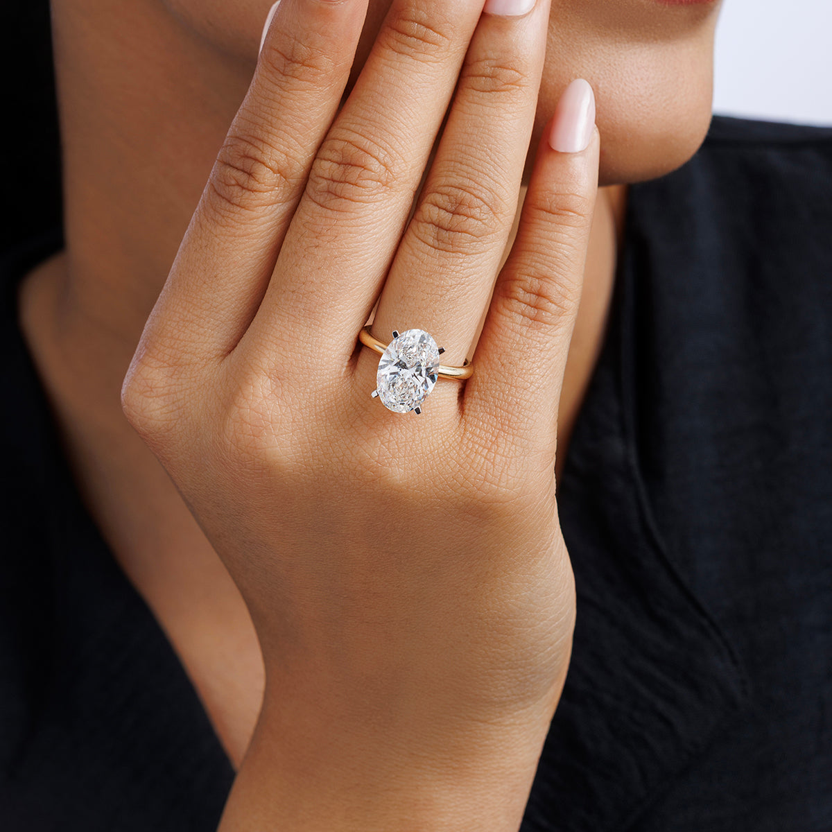 A hand with nude nails shows off the luminous Keemti Jewels MINIMAL Oval Solitaire RING near a smiling face.