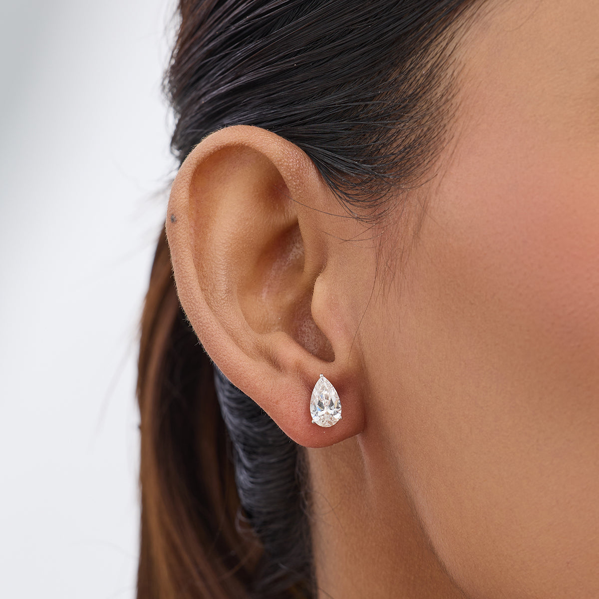 Close-up of a woman’s ear wearing Keemti Jewels PEARLUXE Solitaire Stud Earrings in a teardrop prong setting.