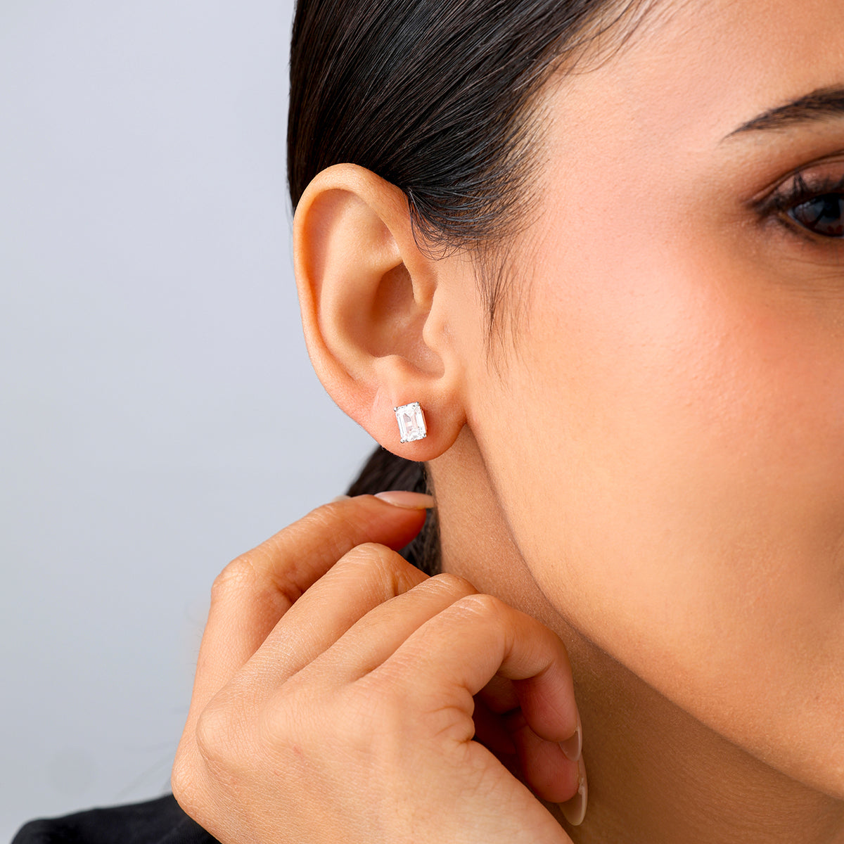 Close-up of a woman wearing Keemti Jewels' EMERALD Solitaire Stud EARRINGS, hand on chin for a timeless touch.