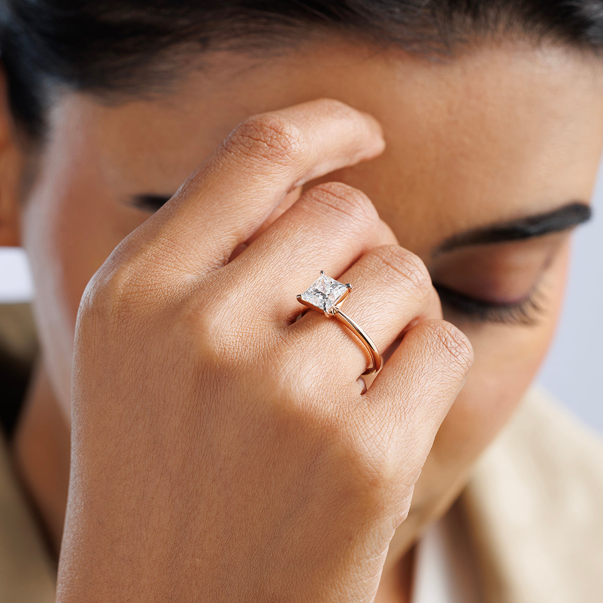 A woman with closed eyes touches her face, wearing Keemti Jewels’ CLASSIC Princess Engagement Ring on her finger.