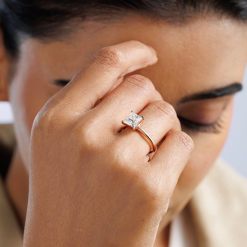 A woman with closed eyes touches her face, wearing Keemti Jewels’ CLASSIC Princess Engagement Ring on her finger.