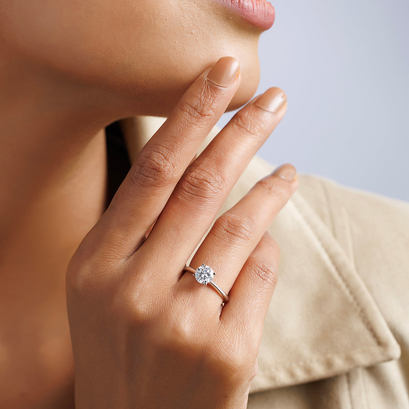 A person displays the Keemti Jewels ELEGANT Round Solitaire RING on their finger against a neutral background.